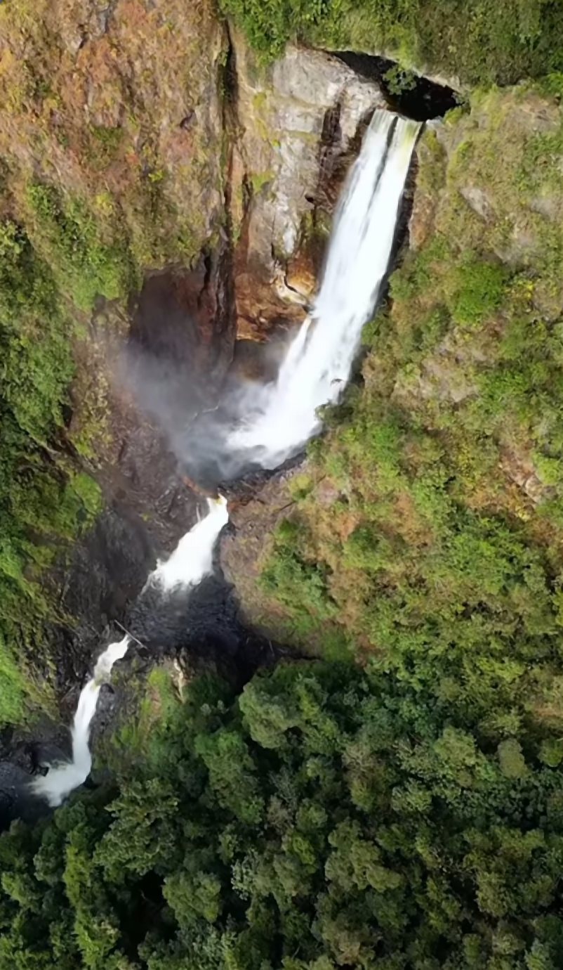 Vista aérea de una cascada alta que cae entre paredes de roca y bosque