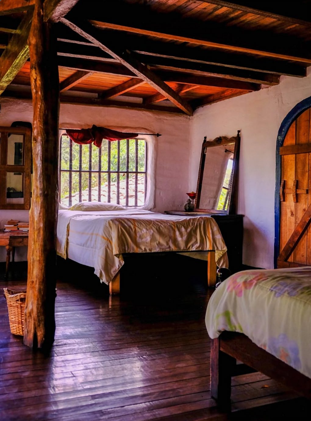 Habitación con vigas de madera, camas individuales, piso de madera y una puerta azul en arco