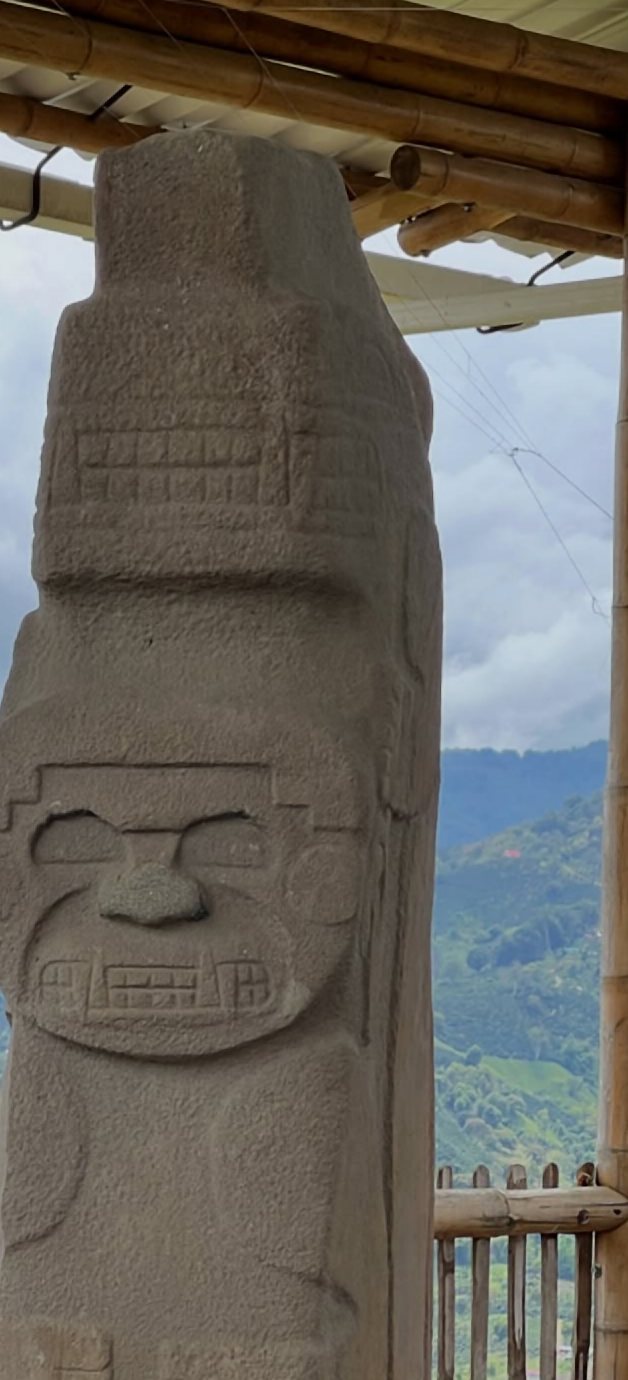 Estatua de piedra con un rostro tallado, frente a montañas verdes, en la región de San Agustín