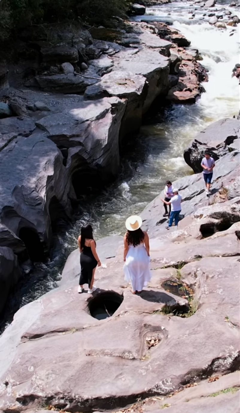 Río caudaloso entre rocas lisas, con visitantes caminando sobre las piedras